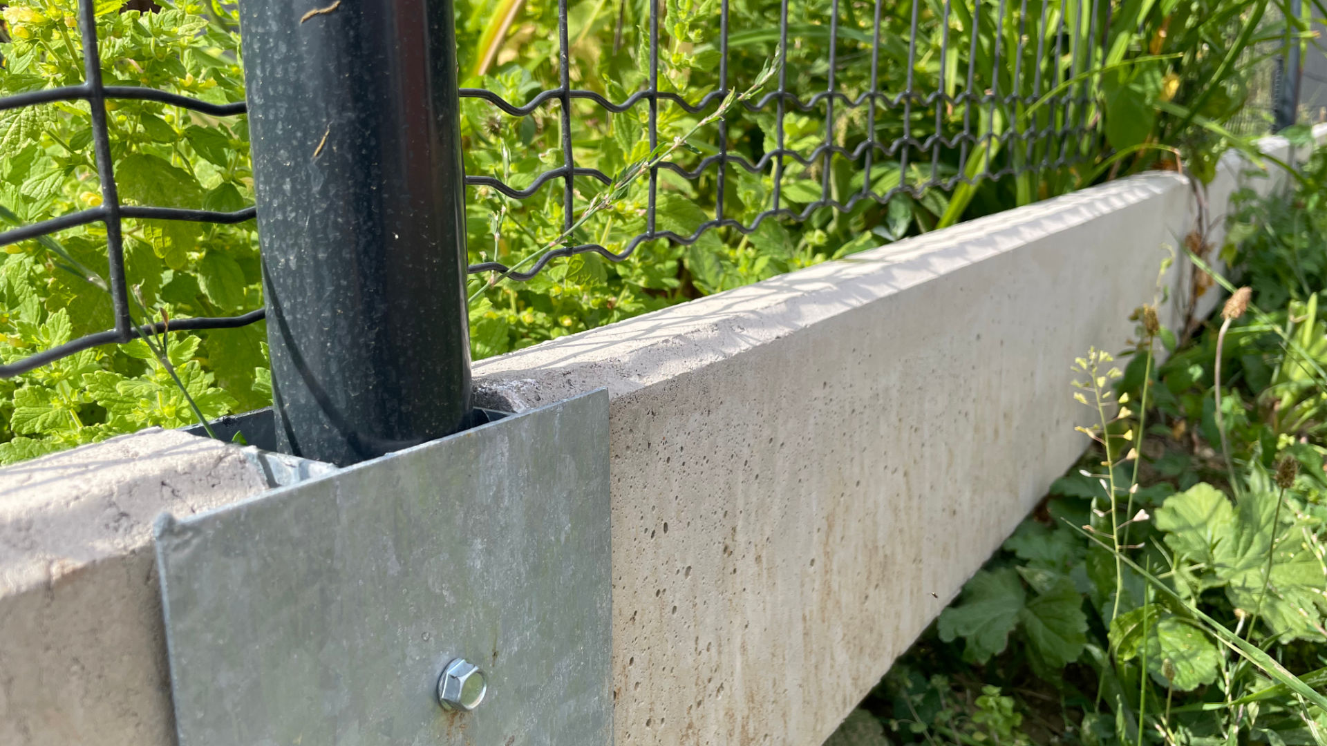 Podhrabová betonová deska pod plot jako náhrada podezdívky – detail uchycení desky v průběžném držáku.