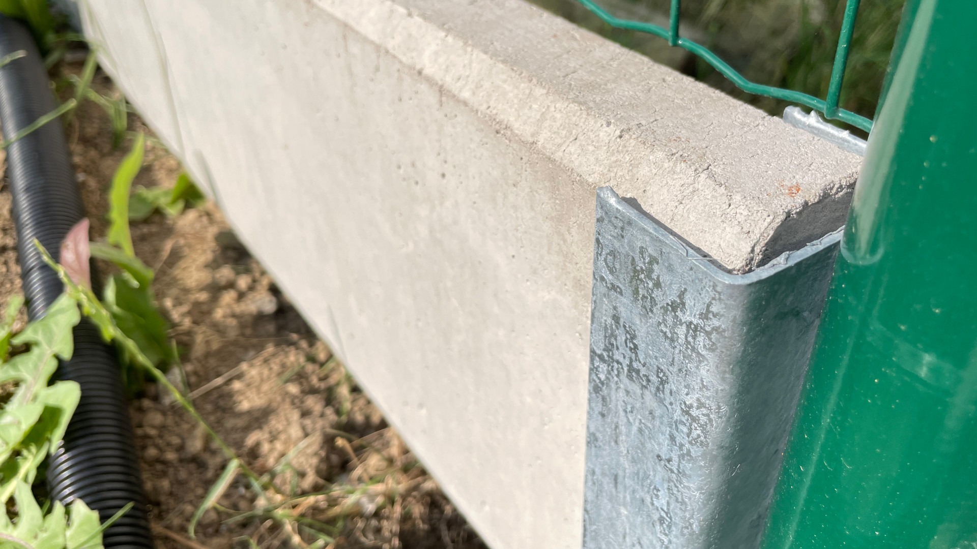 Podhrabová betonová deska pod plot jako náhrada podezdívky – detail uchycení desky v koncovém držáku.